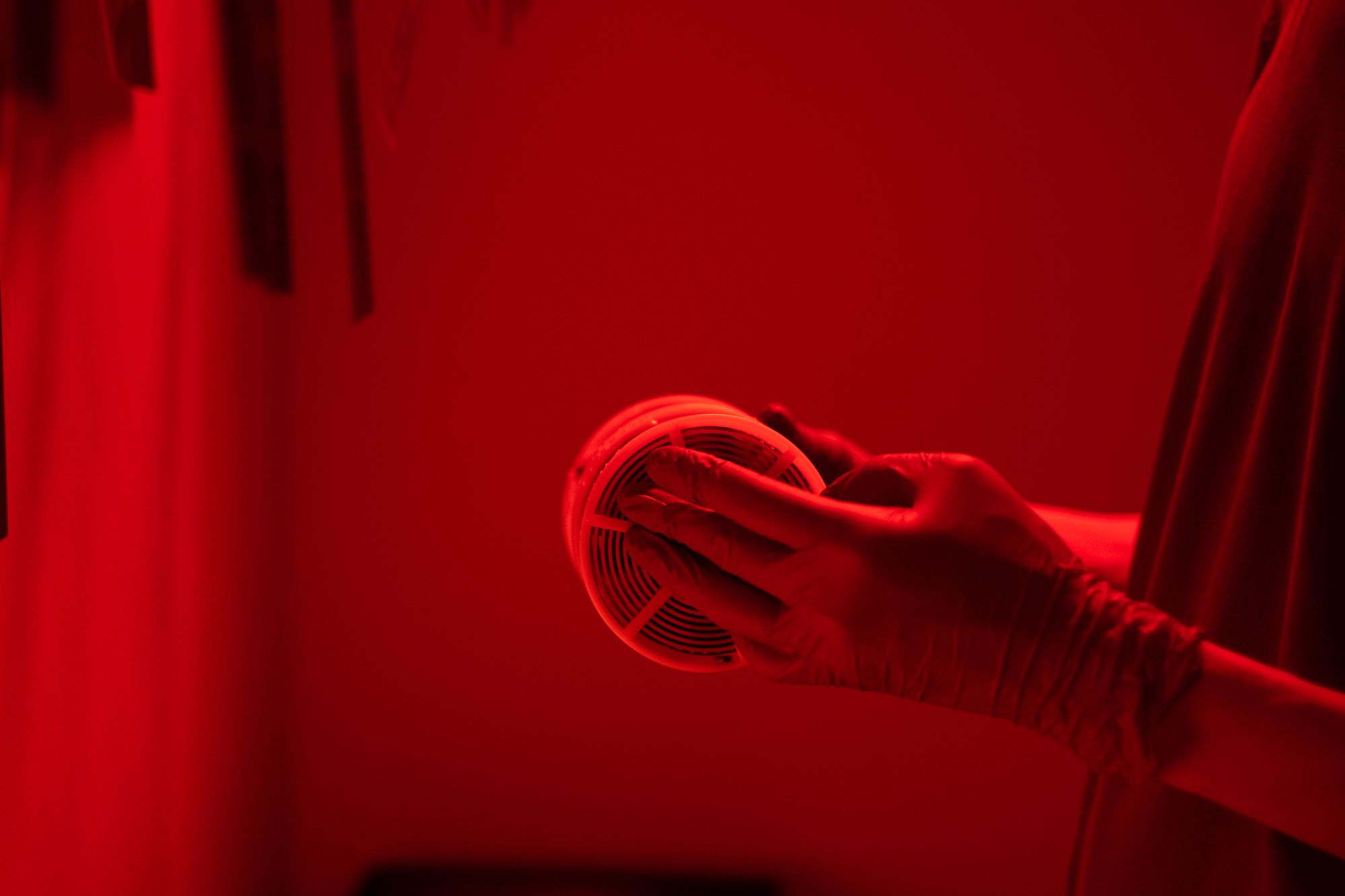 Mano con guante colocando un detector de humo en el techo bajo iluminación roja