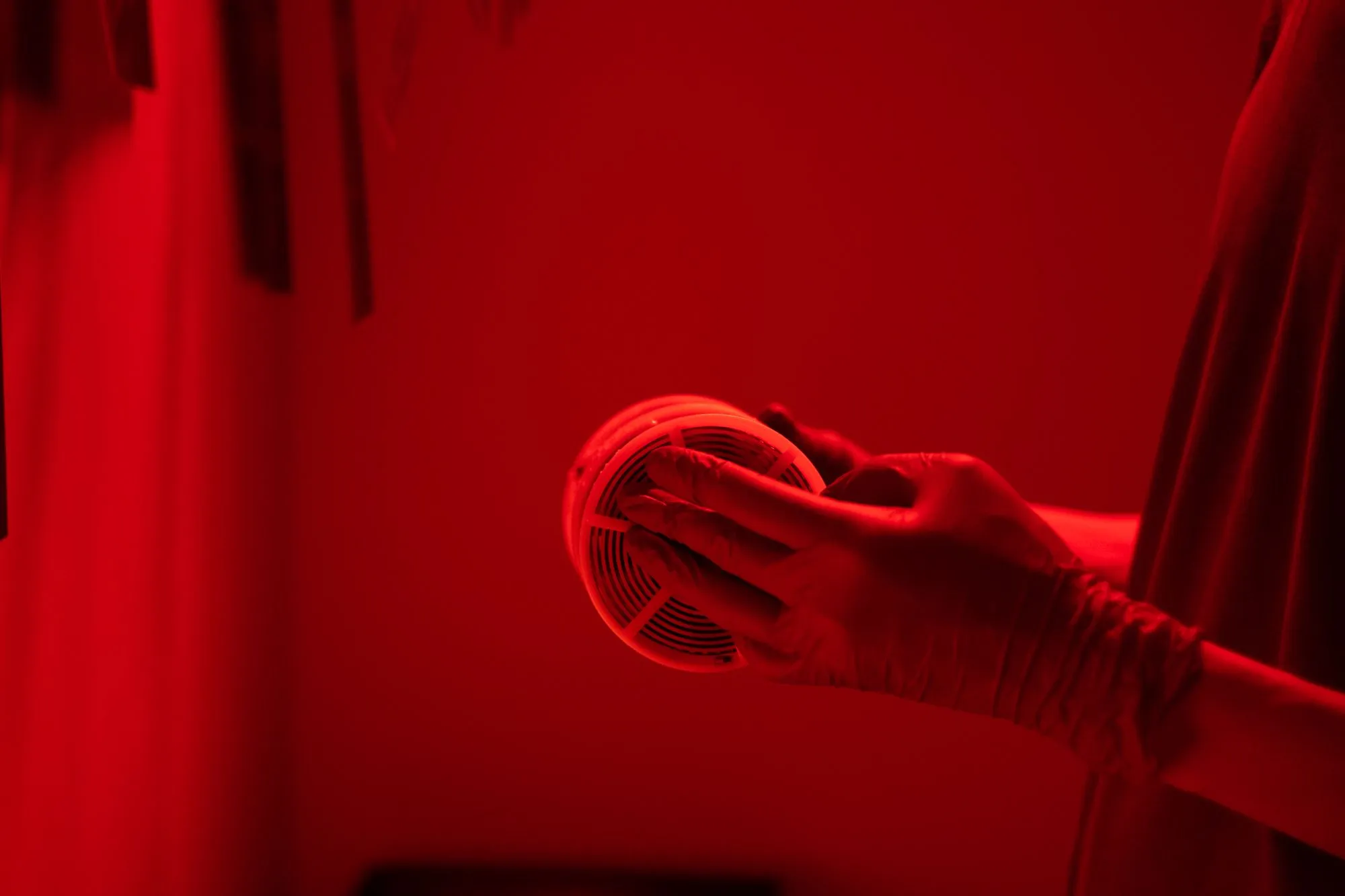 Mano con guante colocando un detector de humo en el techo bajo iluminación roja