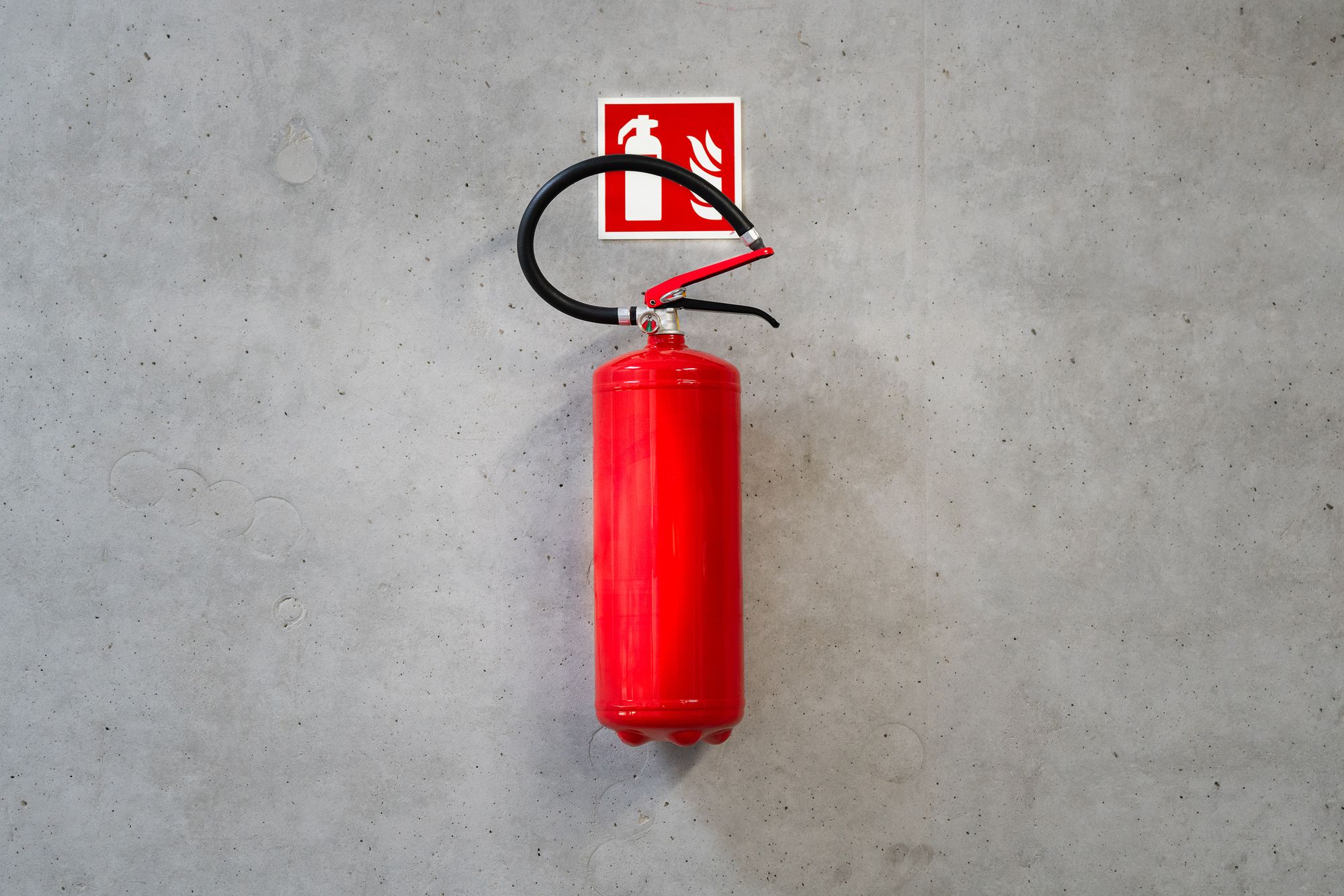 Extintor rojo colgado en un muro de concreto bajo su señal de ubicación