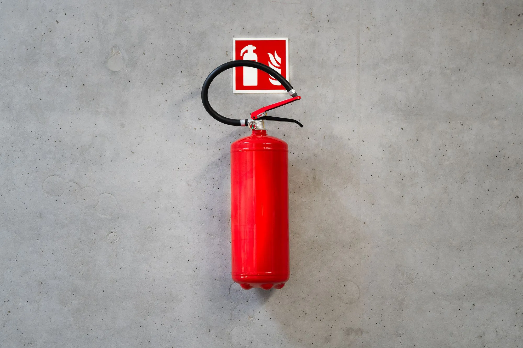 Extintor rojo colgado en un muro de concreto bajo su señal de ubicación